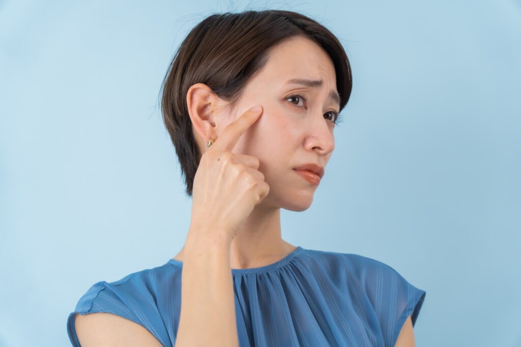 右手人差し指で右顔面を指差し、困った顔をしている女性